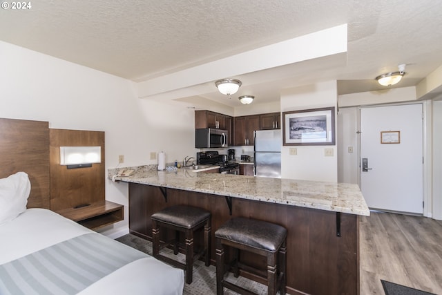 kitchen with light hardwood / wood-style flooring, kitchen peninsula, stainless steel appliances, a breakfast bar area, and light stone countertops