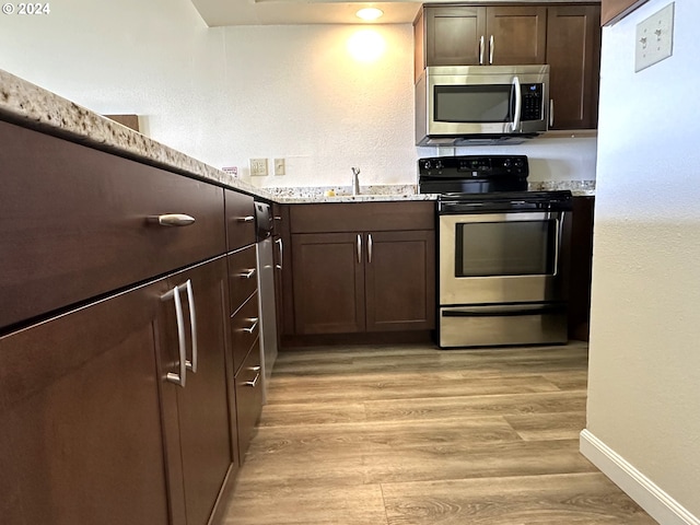 kitchen featuring light stone countertops, light wood-type flooring, range with electric stovetop, dark brown cabinetry, and sink