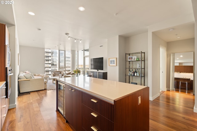 kitchen with beverage cooler, dark brown cabinetry, a large island, light wood-type flooring, and appliances with stainless steel finishes