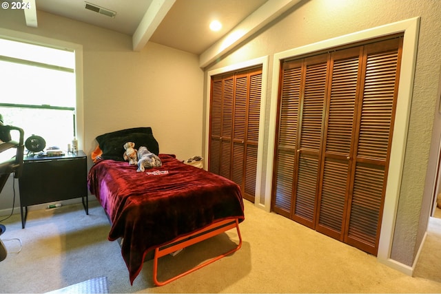 carpeted bedroom featuring vaulted ceiling with beams and multiple closets