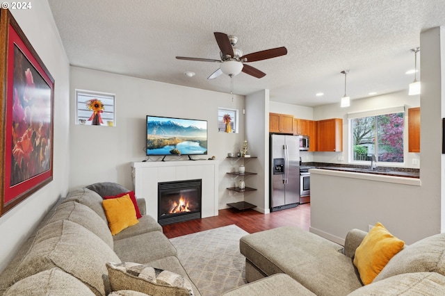 living room with a tile fireplace, sink, ceiling fan, a textured ceiling, and dark hardwood / wood-style flooring