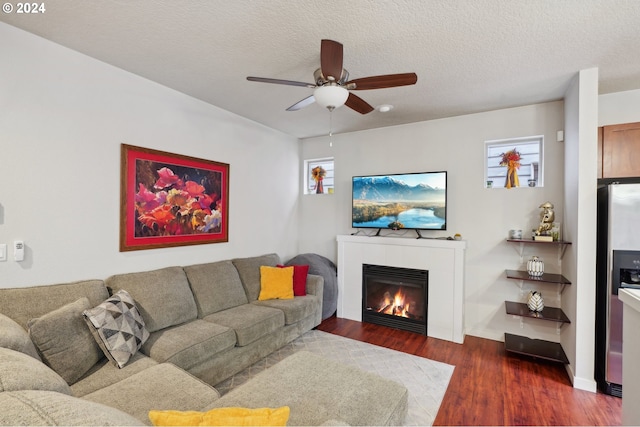 living room with a tile fireplace, ceiling fan, dark wood-type flooring, and a textured ceiling