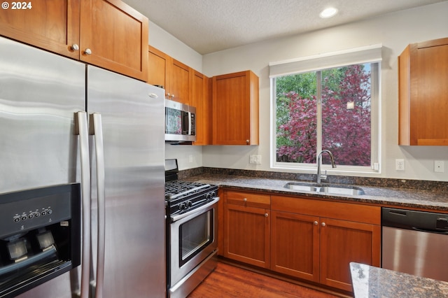 kitchen with dark stone countertops, sink, appliances with stainless steel finishes, and dark wood-type flooring