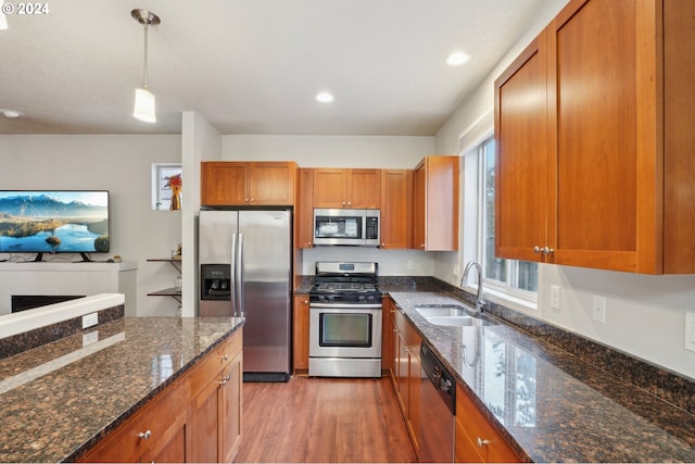 kitchen featuring dark stone counters, stainless steel appliances, sink, pendant lighting, and hardwood / wood-style flooring