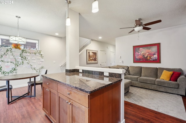 kitchen with ceiling fan, dark hardwood / wood-style floors, dark stone countertops, a textured ceiling, and decorative light fixtures