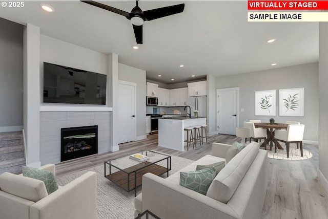 living room featuring ceiling fan, a tiled fireplace, sink, and light hardwood / wood-style flooring