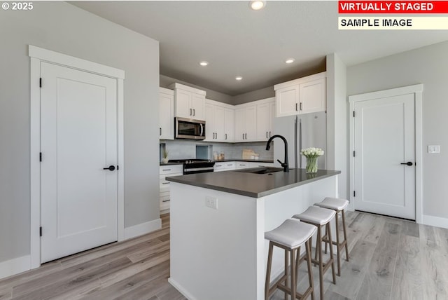 kitchen featuring appliances with stainless steel finishes, a breakfast bar, white cabinetry, sink, and a center island with sink