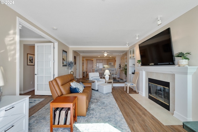 living room with a tiled fireplace, ceiling fan, light hardwood / wood-style floors, and ornamental molding