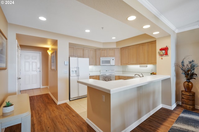 kitchen with light brown cabinets, white appliances, ornamental molding, light hardwood / wood-style floors, and kitchen peninsula