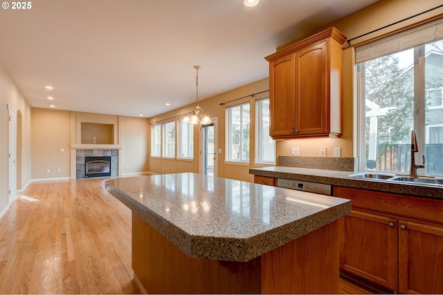 kitchen featuring sink, a center island, hanging light fixtures, a tiled fireplace, and light hardwood / wood-style floors