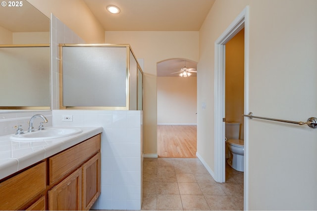 bathroom featuring a shower with shower door, tile patterned flooring, vanity, ceiling fan, and toilet