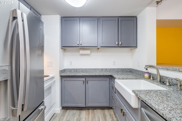 kitchen featuring appliances with stainless steel finishes, light wood-type flooring, light stone counters, and gray cabinets