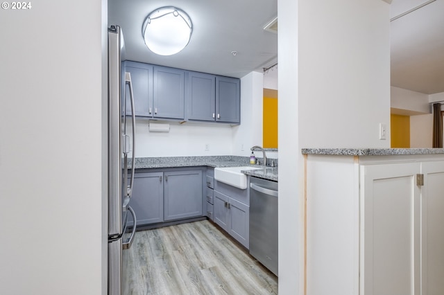 kitchen with stainless steel appliances, gray cabinets, light wood-type flooring, light stone countertops, and sink