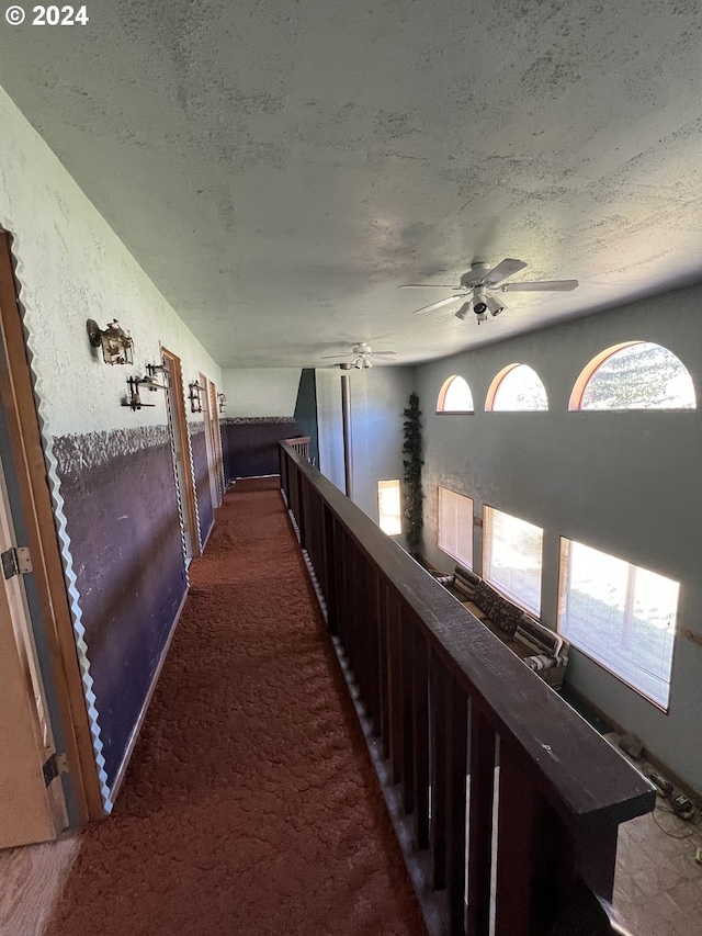 hall with a textured wall, a healthy amount of sunlight, dark carpet, and a textured ceiling