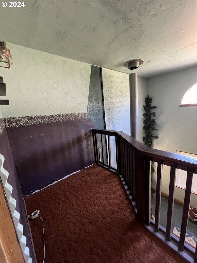 hallway with dark colored carpet, a textured wall, and stairway