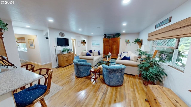 living room with a fireplace with raised hearth, recessed lighting, light wood-type flooring, and baseboards