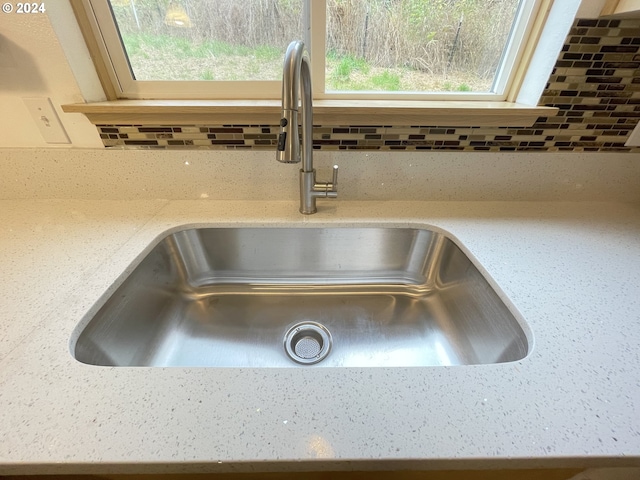 interior details with tasteful backsplash, a sink, and light stone countertops