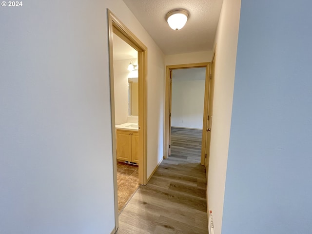 hall featuring light wood-style flooring, baseboards, and a textured ceiling