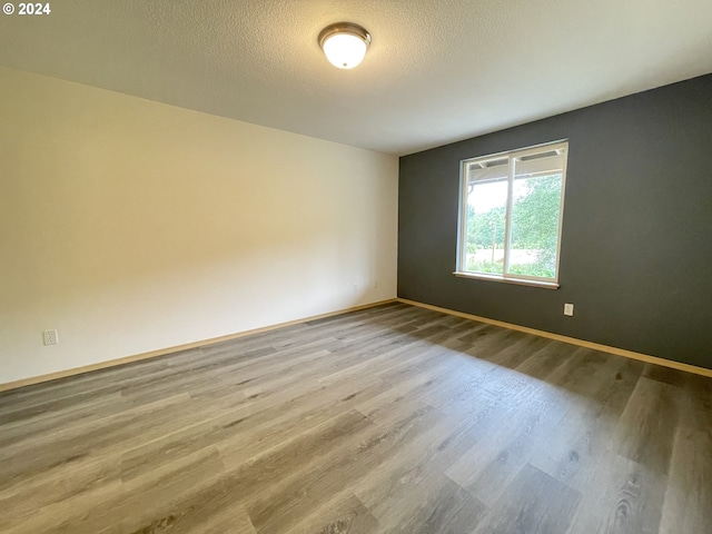 empty room featuring a textured ceiling, baseboards, and wood finished floors