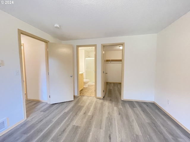 unfurnished bedroom with a walk in closet, a closet, a textured ceiling, and light wood finished floors