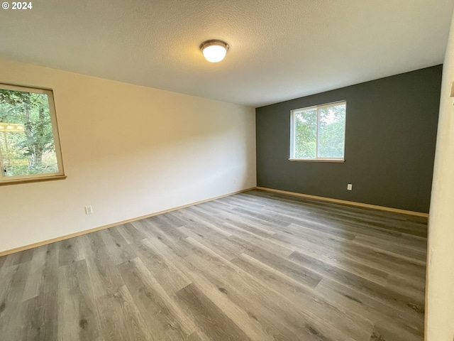 unfurnished room with a textured ceiling, baseboards, and wood finished floors