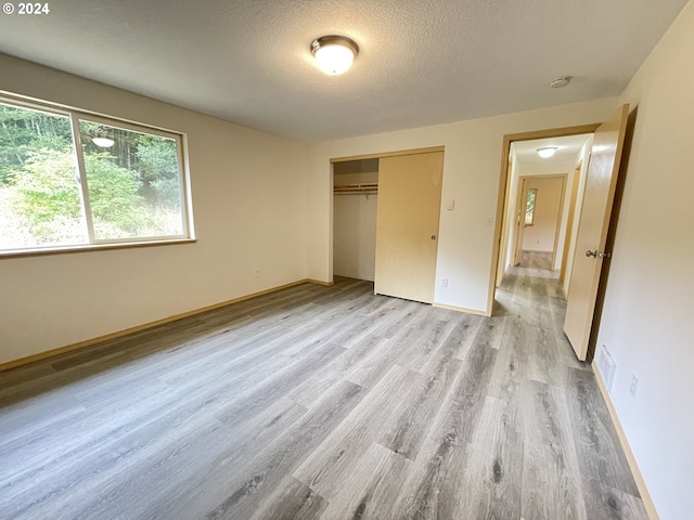 unfurnished bedroom with a textured ceiling, a closet, and light hardwood / wood-style floors