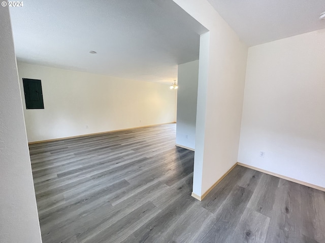 spare room with a notable chandelier, electric panel, baseboards, and wood finished floors