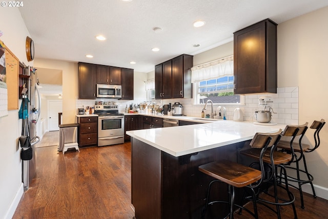 kitchen with tasteful backsplash, kitchen peninsula, dark wood-type flooring, stainless steel appliances, and sink