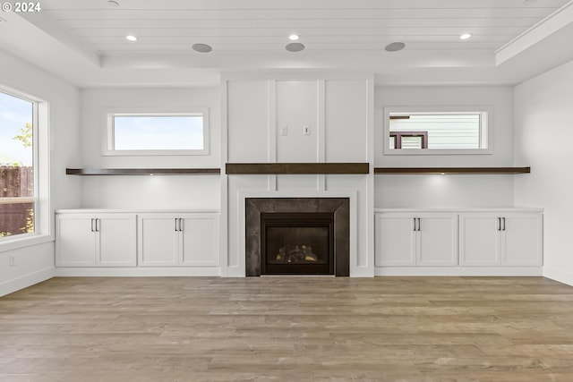 unfurnished living room featuring a premium fireplace, a wealth of natural light, a raised ceiling, and light hardwood / wood-style flooring