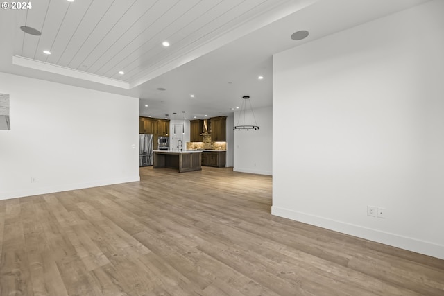 unfurnished living room featuring a tray ceiling, sink, and light hardwood / wood-style floors