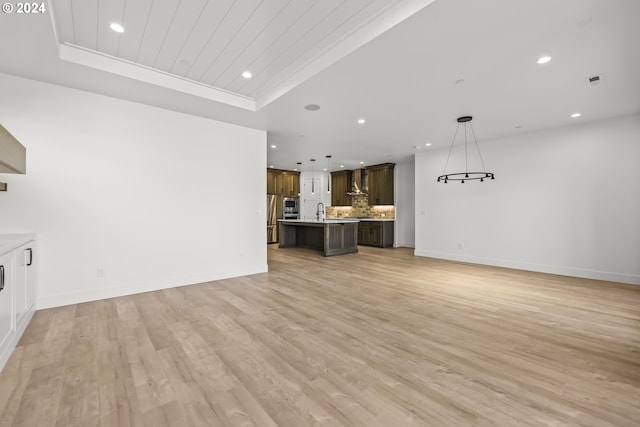 unfurnished living room with light hardwood / wood-style floors, sink, and a raised ceiling