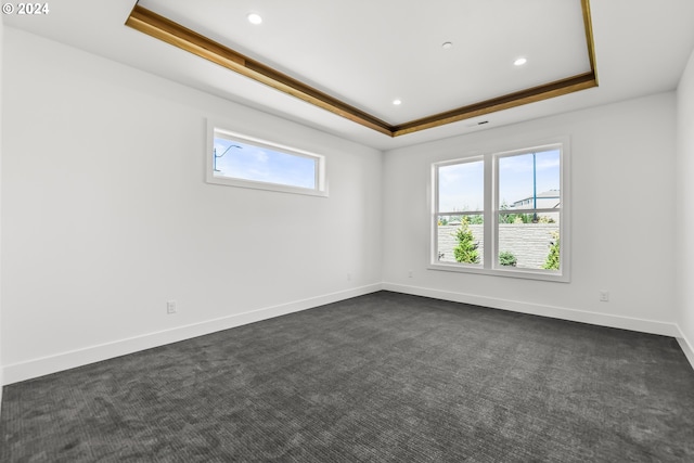 spare room with a tray ceiling and dark carpet