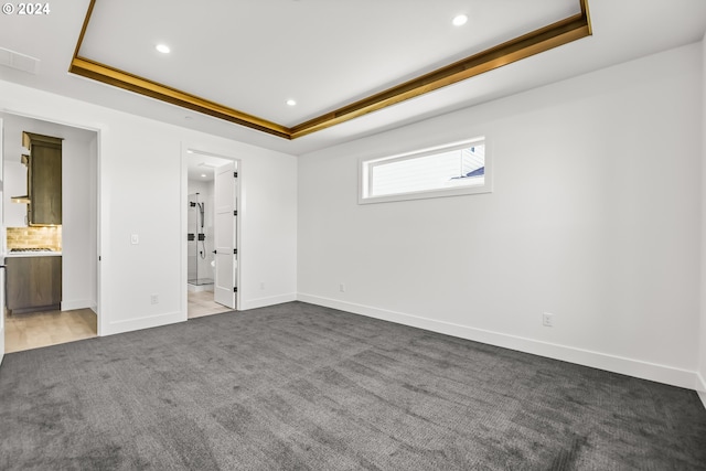 interior space with a tray ceiling, carpet flooring, and connected bathroom