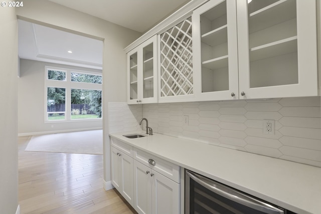 bar with tasteful backsplash, light hardwood / wood-style flooring, beverage cooler, sink, and white cabinets