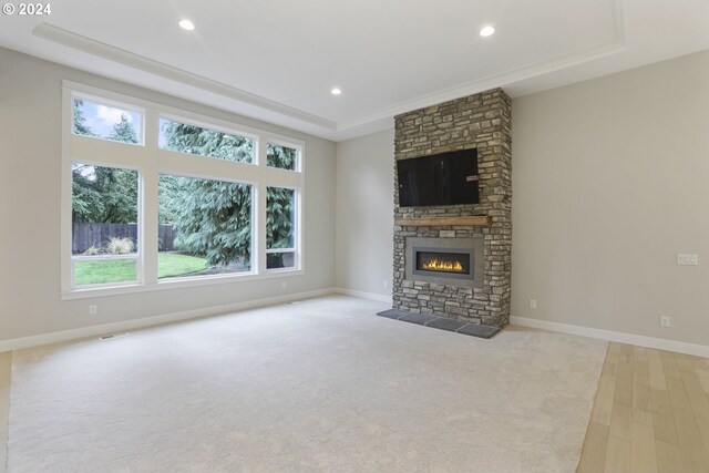 unfurnished living room with a tray ceiling, light carpet, and a stone fireplace