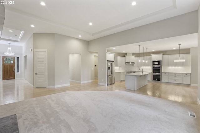 unfurnished living room featuring a raised ceiling, sink, and light hardwood / wood-style floors