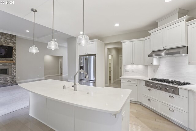 kitchen with a center island with sink, a stone fireplace, appliances with stainless steel finishes, tasteful backsplash, and white cabinets