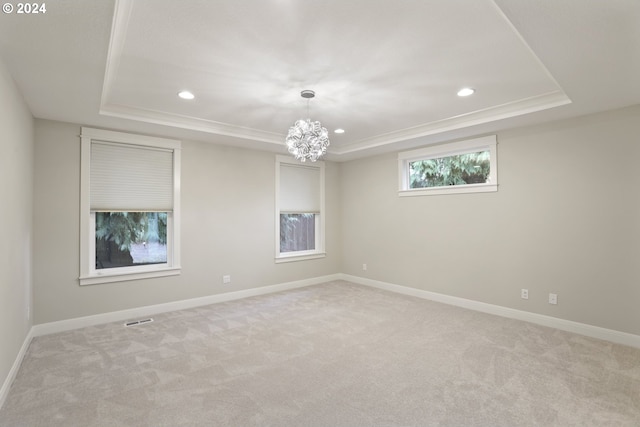 carpeted spare room featuring a raised ceiling and a notable chandelier