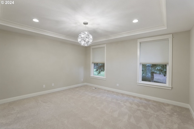 carpeted spare room featuring a raised ceiling and an inviting chandelier