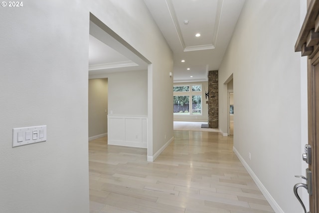 hall with a raised ceiling, brick wall, and light hardwood / wood-style floors