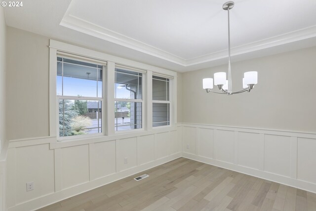 unfurnished dining area with light wood-type flooring, a raised ceiling, ornamental molding, and a notable chandelier