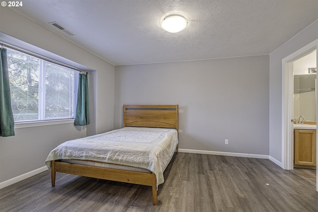 bedroom with connected bathroom, sink, dark hardwood / wood-style floors, and a textured ceiling