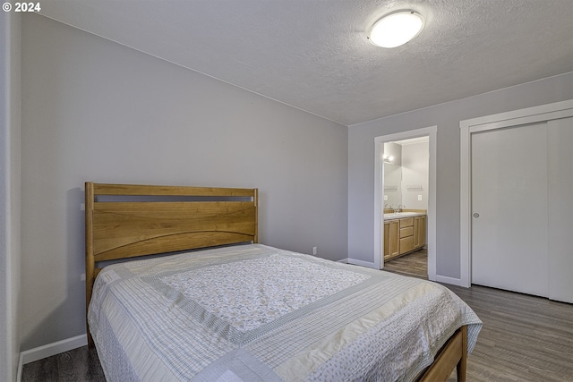 bedroom with sink, hardwood / wood-style flooring, a textured ceiling, connected bathroom, and a closet