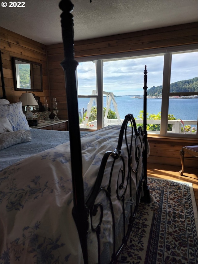 bedroom featuring wood walls, a water view, a textured ceiling, and hardwood / wood-style flooring