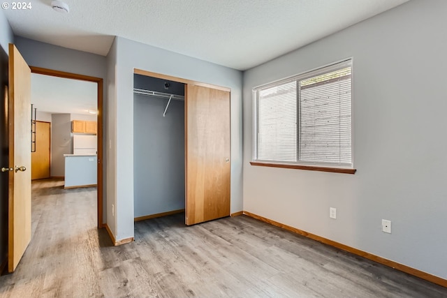 unfurnished bedroom featuring fridge, a textured ceiling, a closet, and light wood-type flooring