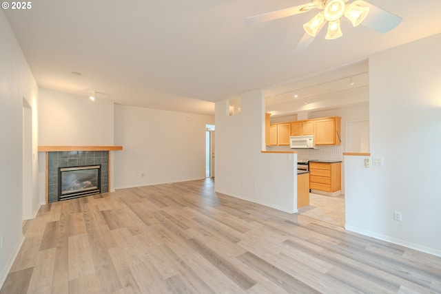 unfurnished living room featuring light wood finished floors, ceiling fan, baseboards, and a fireplace