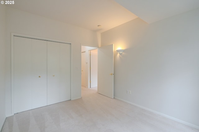 unfurnished bedroom with a closet, light colored carpet, and baseboards