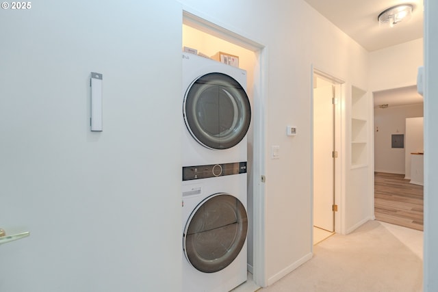 clothes washing area with baseboards, light colored carpet, stacked washer / drying machine, and laundry area