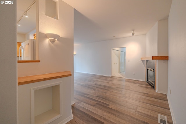 unfurnished living room with visible vents, baseboards, a fireplace, wood finished floors, and rail lighting