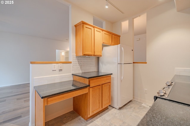 kitchen with freestanding refrigerator, rail lighting, tasteful backsplash, dark stone countertops, and baseboards